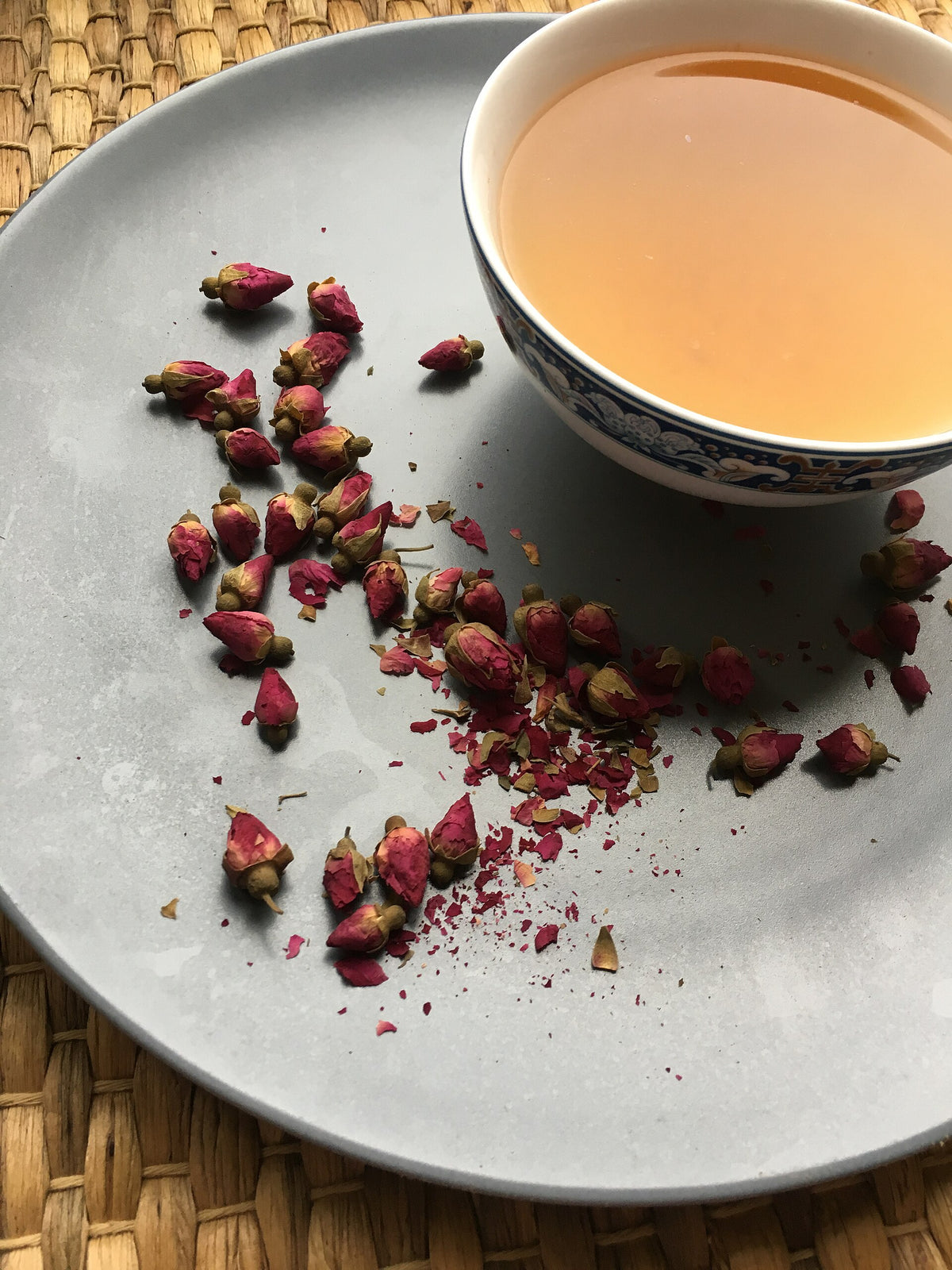 A cup of rosebud tea surrounded by dried pink rose buds, ideal as a gift